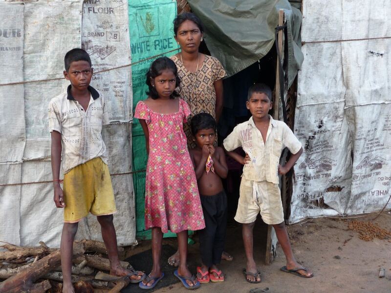 Eine Familie mit vier Kindern steht vor einer provisorischen Unterkunft aus Planen und Säcken